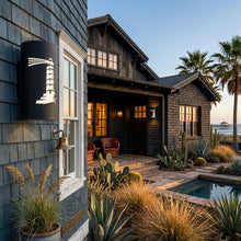 Load image into Gallery viewer, Lighthouse wall sconce in black, mounted beside a window on a shingled beach house at dusk